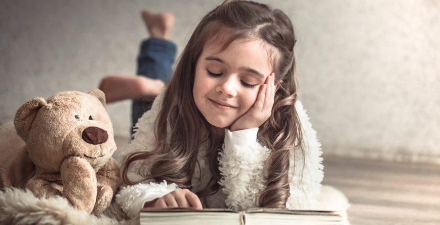 little girl reading a book with a Teddy bear on the floor in a cozy living room at home, beautiful emotions, the concept of relaxation and friendship