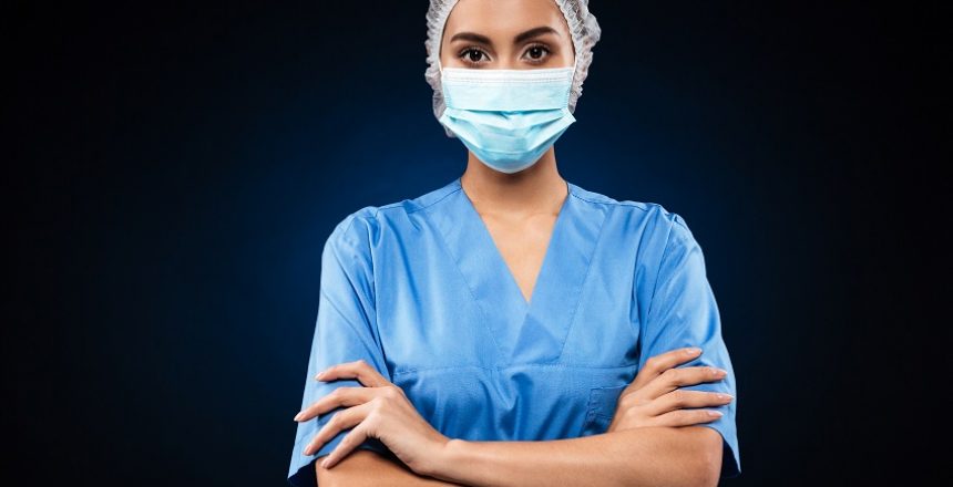 Serious doctor in medical mask and cap looking camera and holding hands folded isolated over black