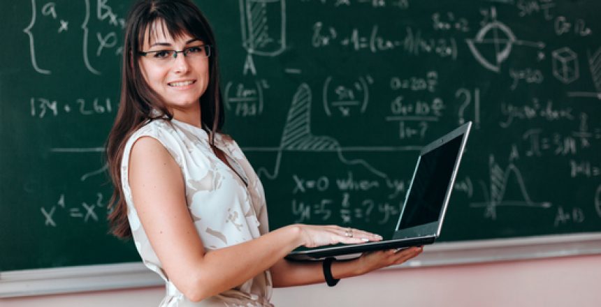 Woman teacher in glasses holding open laptop and looking at the camera. Back to school