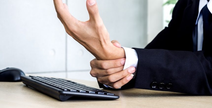 Close-up businessman in suit getting hand pain while using notebook computer in office. Suffering from work-related pain and office syndrome concept.