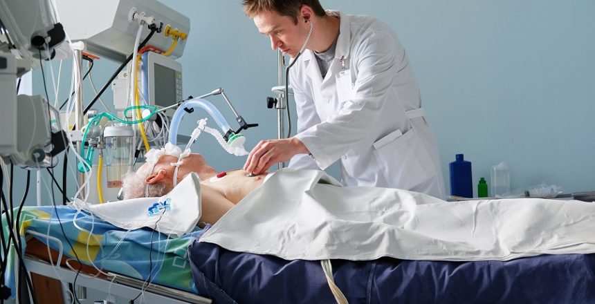 Intensive care caucasian doctor examines intubated critical stance patient in intensive care department. Doctor at work.