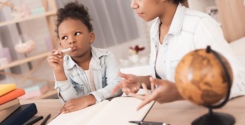 Mom and daughter together do their homework in school. They are both mulattoes. Mom helps a little girl learn.