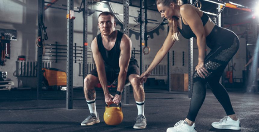 Athletic man and woman with a dumbbells training and practicing in gym. Concept of sport, healthy lifestyle, wellbeing.